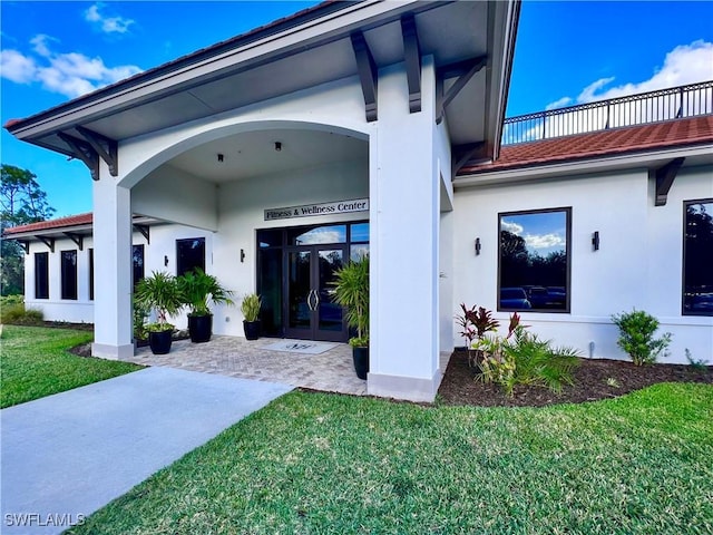 doorway to property featuring stucco siding, a lawn, and french doors