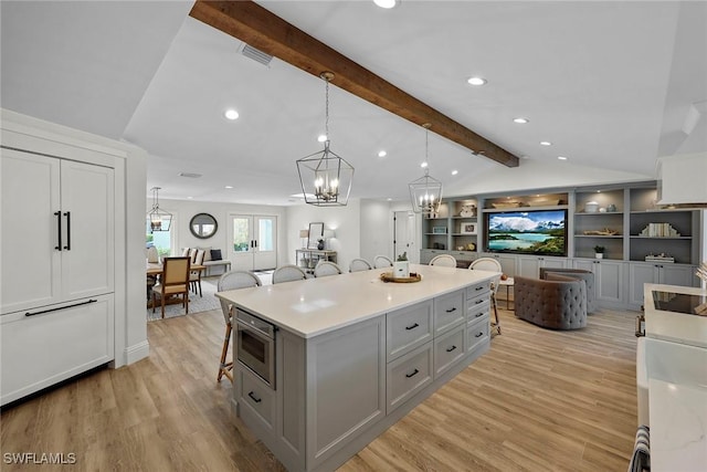 kitchen with a kitchen bar, a center island, lofted ceiling with beams, hanging light fixtures, and gray cabinets