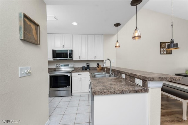 kitchen with stainless steel appliances, dark countertops, a sink, and a peninsula