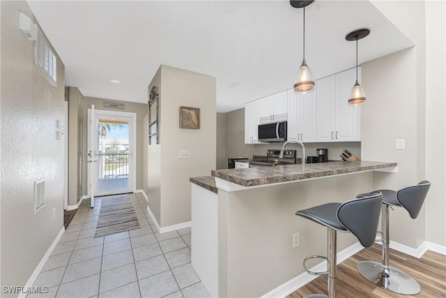 kitchen featuring visible vents, dark countertops, appliances with stainless steel finishes, a breakfast bar, and white cabinetry