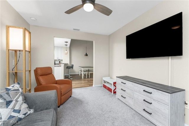 living room featuring light colored carpet, visible vents, ceiling fan, and baseboards