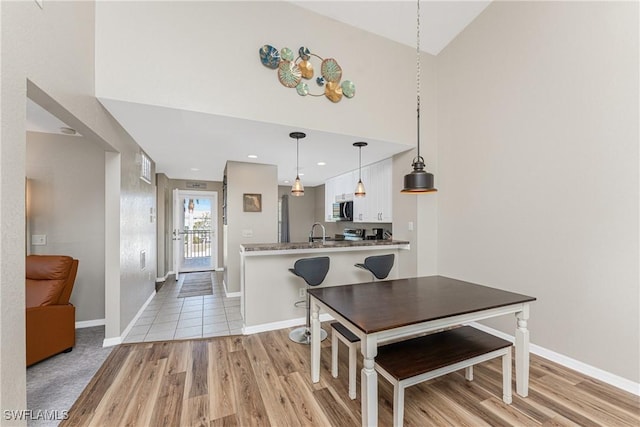 dining room featuring a high ceiling, light wood-style flooring, and baseboards