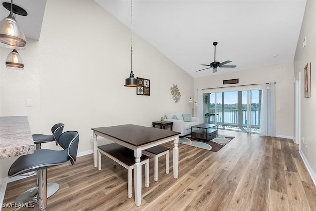 dining room with ceiling fan, high vaulted ceiling, light wood-type flooring, and baseboards