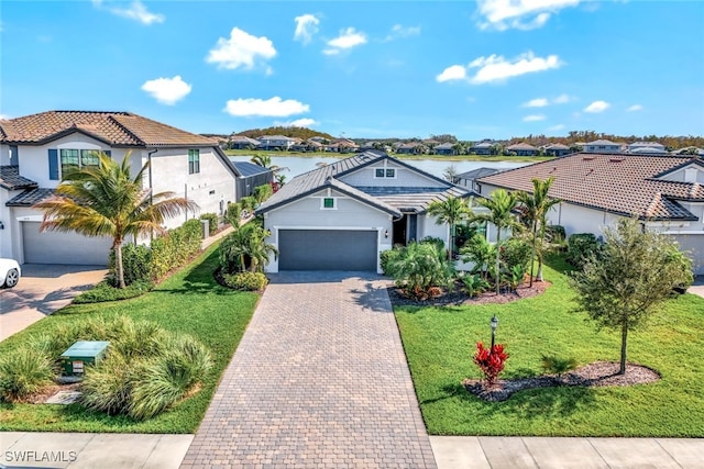 view of front facade featuring a water view, an attached garage, a residential view, and decorative driveway