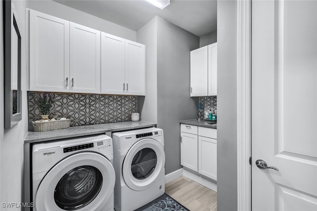 laundry area with light wood-type flooring, washing machine and dryer, cabinet space, and baseboards