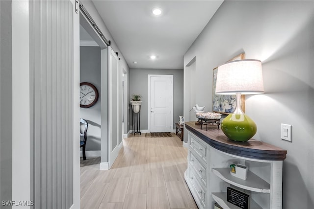 hall featuring a barn door, baseboards, light wood-style flooring, and recessed lighting