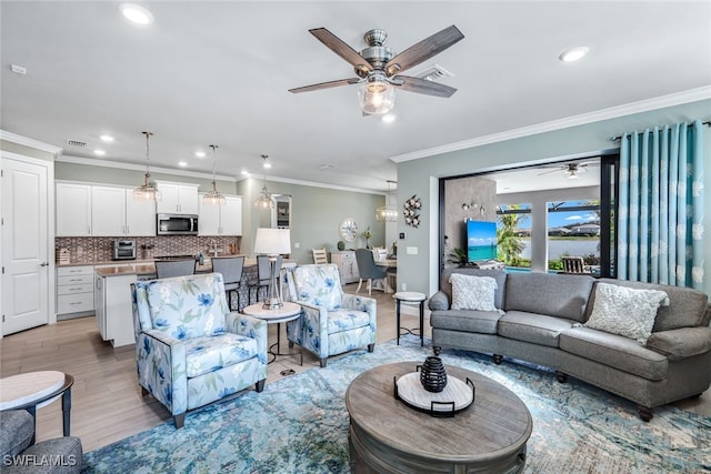 living room with ornamental molding, light wood-type flooring, visible vents, and ceiling fan