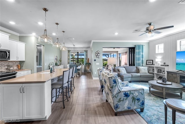 living area with ceiling fan, ornamental molding, and baseboards