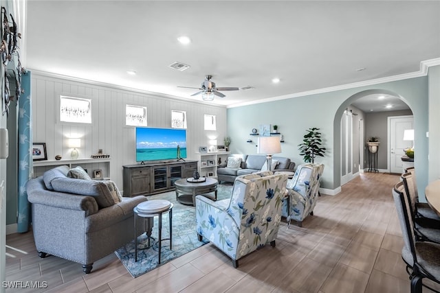 living area featuring arched walkways, wood finish floors, visible vents, ornamental molding, and ceiling fan