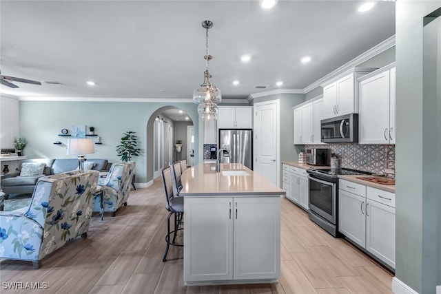 kitchen featuring decorative light fixtures, stainless steel appliances, open floor plan, a kitchen island with sink, and white cabinets