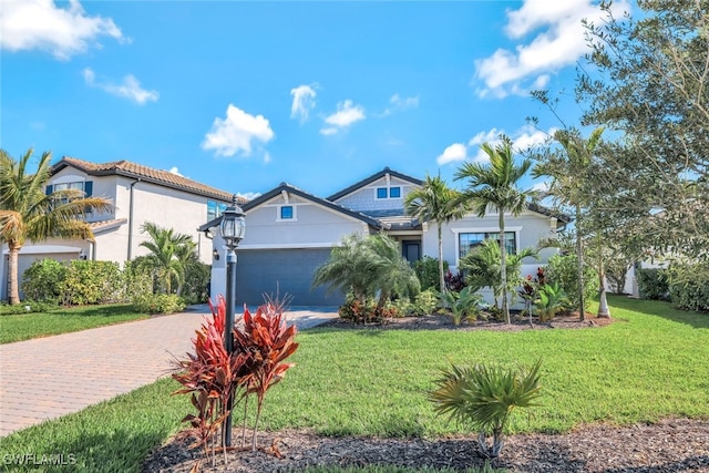 view of front of house featuring decorative driveway, stucco siding, a garage, a tiled roof, and a front lawn