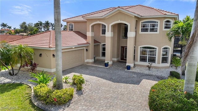 mediterranean / spanish-style house with a garage, a tiled roof, decorative driveway, and stucco siding