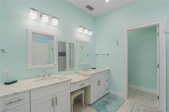 bathroom with visible vents, vanity, baseboards, and wood finished floors