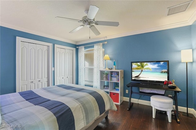 bedroom with baseboards, visible vents, ornamental molding, wood finished floors, and two closets