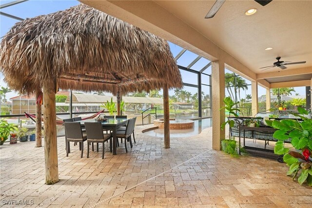 view of patio / terrace featuring a lanai, ceiling fan, a pool with connected hot tub, and outdoor dining space