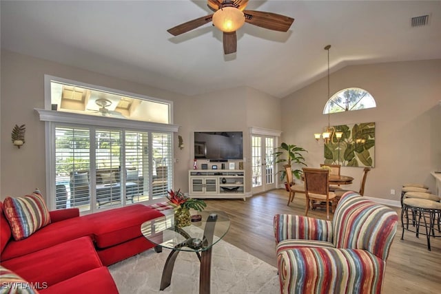 living room with ceiling fan with notable chandelier, vaulted ceiling, french doors, and light wood-type flooring