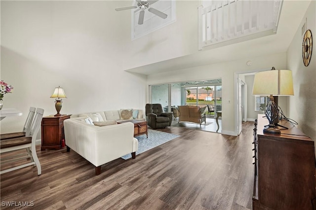 living room featuring dark wood-type flooring, ceiling fan, and a towering ceiling