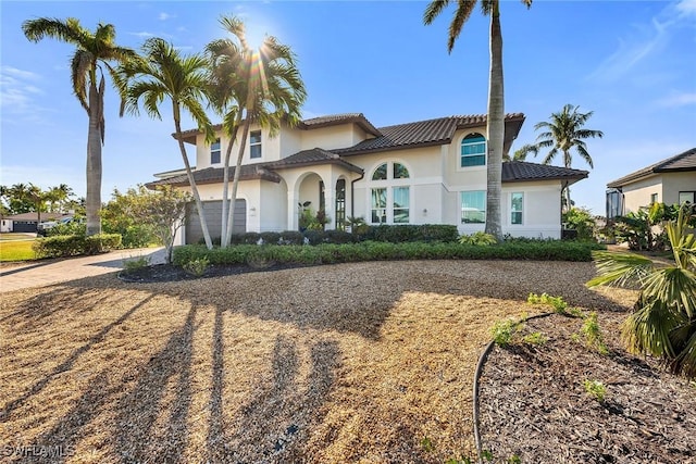 mediterranean / spanish-style home featuring stucco siding, an attached garage, a tile roof, and driveway