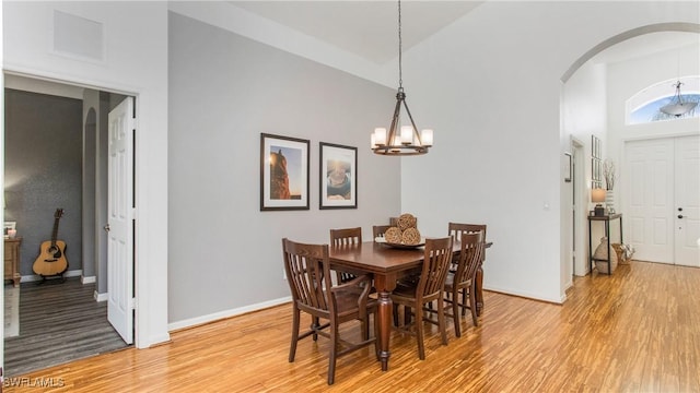 dining area featuring a towering ceiling, a chandelier, and light wood-type flooring