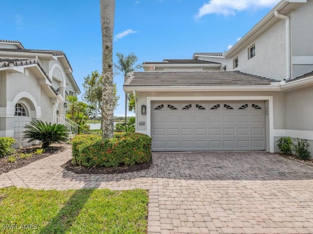 view of side of home featuring decorative driveway, an attached garage, a tile roof, and stucco siding