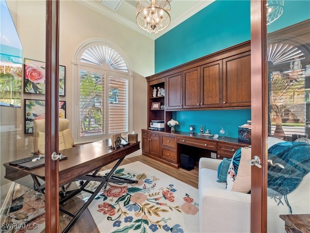 office featuring crown molding, built in desk, an inviting chandelier, and light hardwood / wood-style flooring