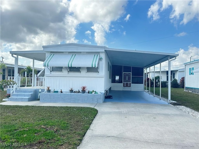 manufactured / mobile home with a front yard, concrete driveway, and an attached carport