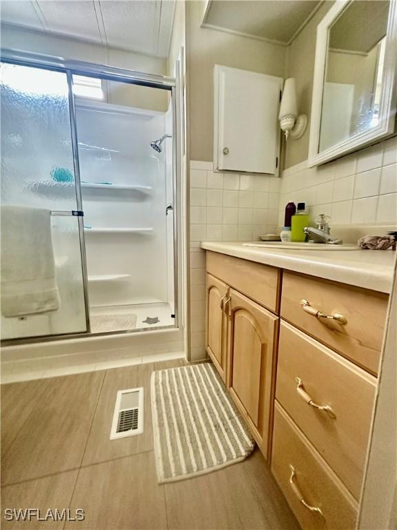 full bathroom with vanity, a shower stall, visible vents, and tile walls