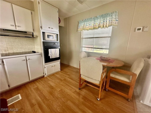 kitchen with under cabinet range hood, white cabinetry, light wood-style floors, visible vents, and black appliances