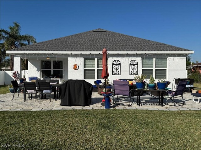 back of house featuring a patio area, roof with shingles, and a lawn