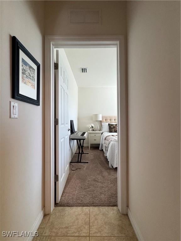 hallway featuring light carpet, baseboards, and visible vents