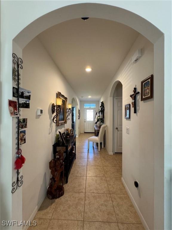 hallway with light tile patterned floors, baseboards, and arched walkways