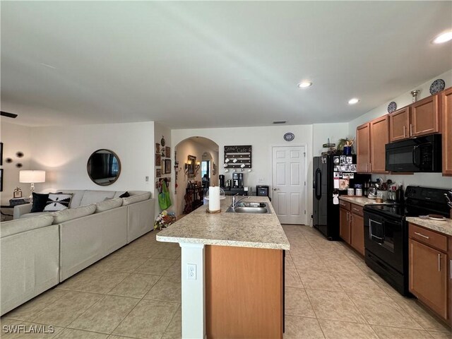 kitchen featuring arched walkways, a center island with sink, light countertops, open floor plan, and black appliances