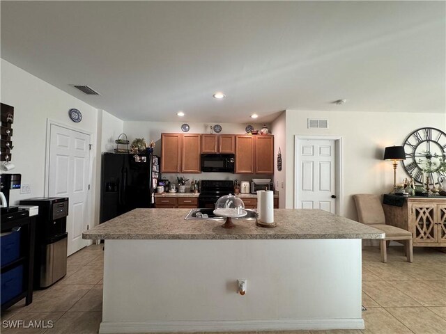 kitchen featuring black appliances, a kitchen island with sink, visible vents, and brown cabinetry