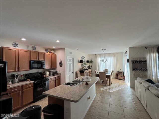 kitchen with light countertops, brown cabinetry, open floor plan, an island with sink, and black appliances