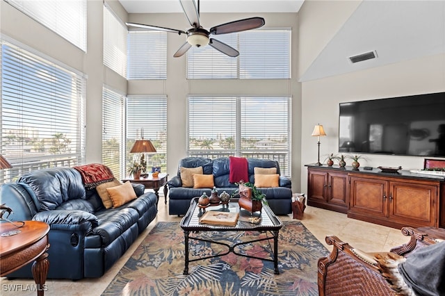 living room with ceiling fan, a towering ceiling, light tile patterned flooring, and a healthy amount of sunlight