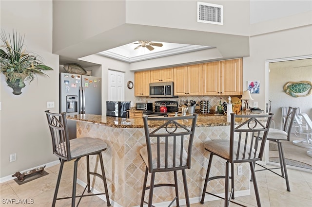 kitchen with kitchen peninsula, appliances with stainless steel finishes, stone counters, and a breakfast bar