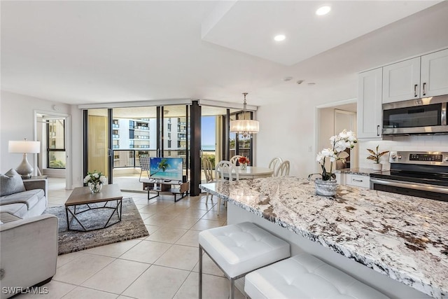 kitchen with appliances with stainless steel finishes, light stone counters, decorative backsplash, white cabinets, and decorative light fixtures