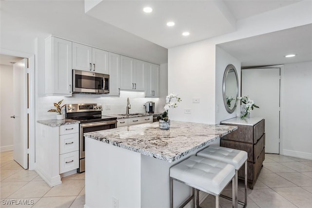 kitchen featuring light stone counters, stainless steel appliances, a kitchen breakfast bar, and white cabinets