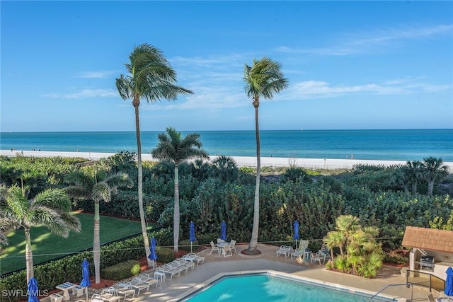 view of swimming pool with a water view, a view of the beach, and a patio area