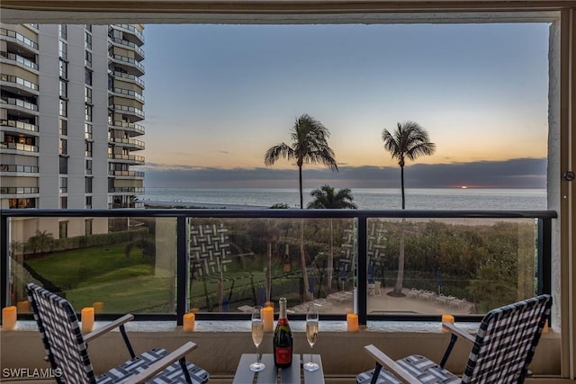 balcony at dusk featuring a water view