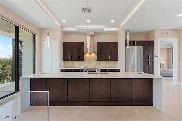 kitchen featuring pendant lighting, sink, stainless steel fridge, a large island with sink, and wall chimney exhaust hood