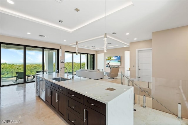 kitchen featuring sink, decorative light fixtures, a tray ceiling, light stone countertops, and a kitchen island with sink