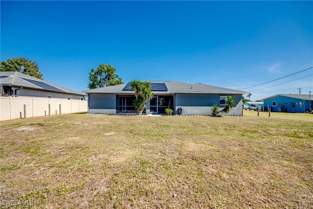 rear view of house featuring a lawn and solar panels