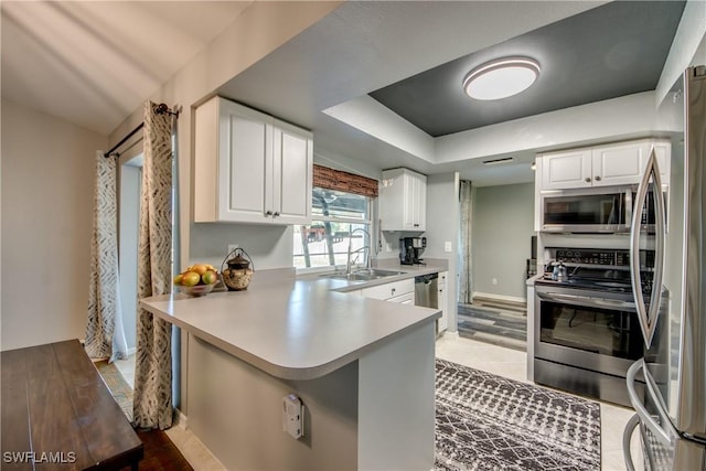 kitchen with appliances with stainless steel finishes, a raised ceiling, sink, white cabinetry, and kitchen peninsula