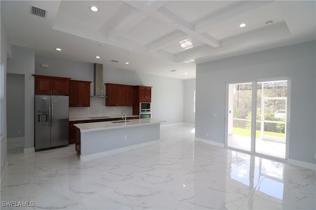 kitchen featuring an island with sink, stainless steel fridge, decorative backsplash, coffered ceiling, and wall chimney range hood