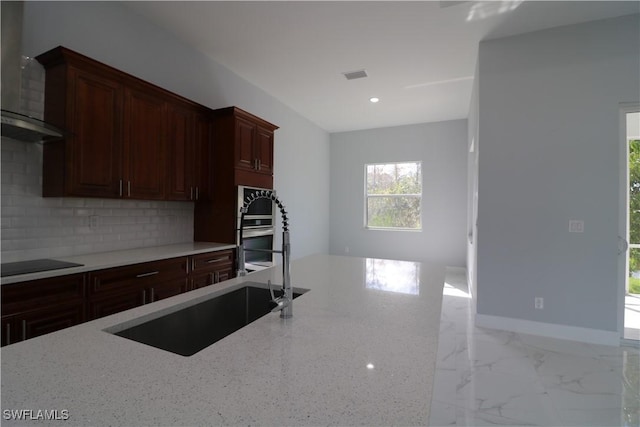 kitchen with wall chimney exhaust hood, black electric stovetop, light stone countertops, and sink