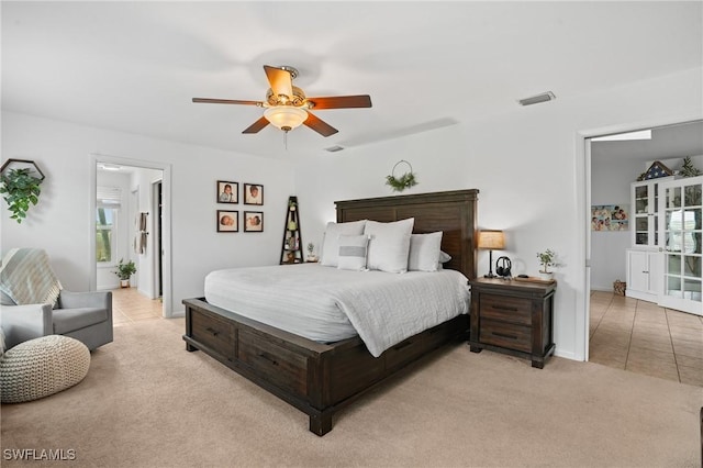 bedroom with a ceiling fan, light carpet, visible vents, and light tile patterned floors