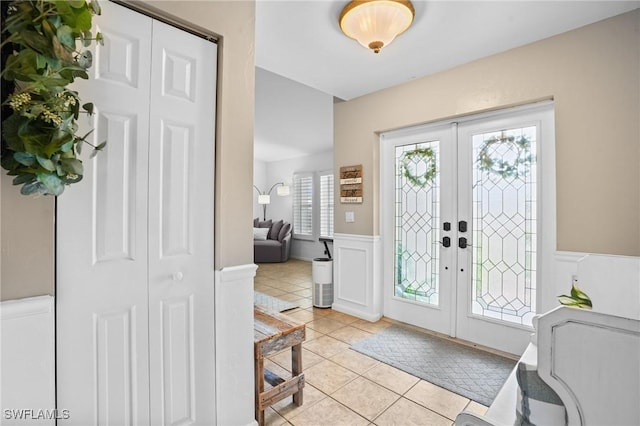 foyer with french doors, a wainscoted wall, a decorative wall, and light tile patterned flooring