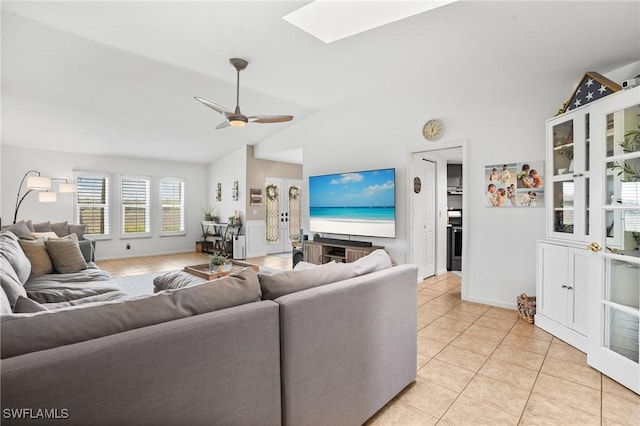 living area featuring light tile patterned floors, vaulted ceiling with skylight, a ceiling fan, and baseboards