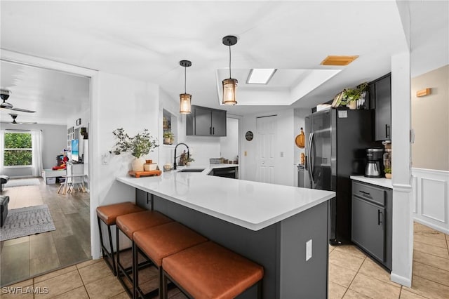 kitchen featuring a breakfast bar, freestanding refrigerator, a peninsula, light countertops, and a sink